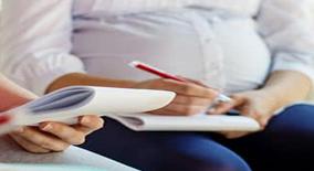 Gros plan sur une femme enceinte assise, tenant des documents et écrivant avec un stylo, illustrant la préparation administrative ou le suivi médical pendant la grossesse.